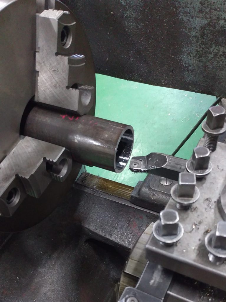ベアリング内輪を押すための治具を旋盤で製作しているところの写真です。固定された円柱型の鉄の棒を、刃物で削って管状に加工していきます。